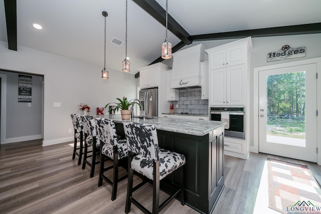 kitchen featuring white cabinetry, hanging light fixtures, backsplash, a large island with sink, and appliances with stainless steel finishes