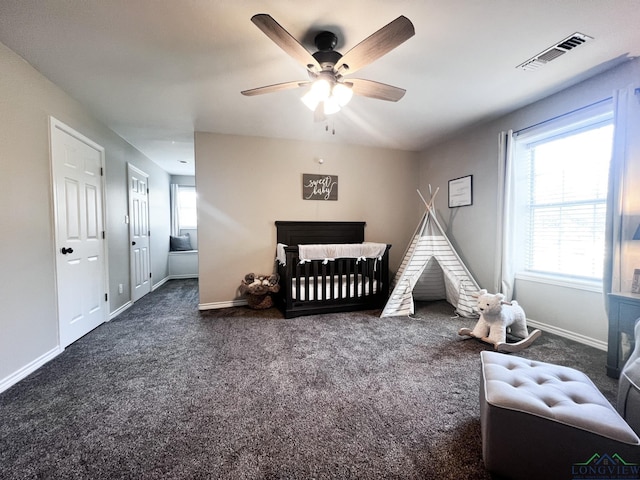 carpeted bedroom with a ceiling fan, a crib, visible vents, and baseboards