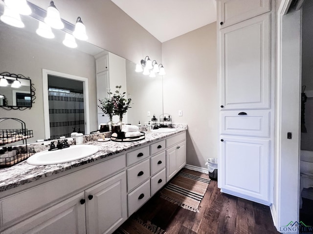 full bath featuring double vanity, wood finished floors, a sink, and baseboards