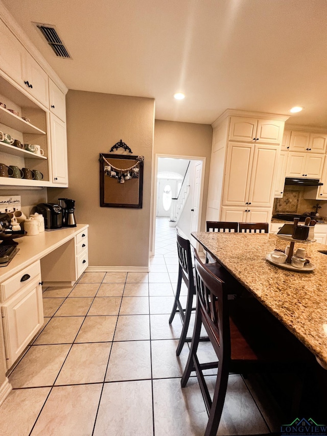 kitchen featuring light tile patterned floors, visible vents, built in study area, light stone countertops, and a kitchen bar