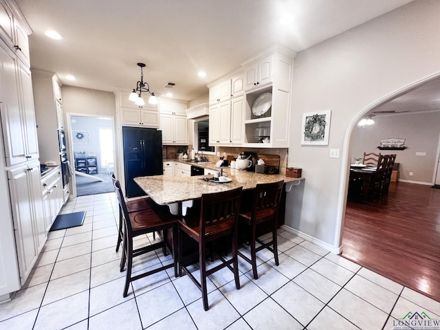 kitchen featuring arched walkways, a peninsula, white cabinetry, open shelves, and black fridge