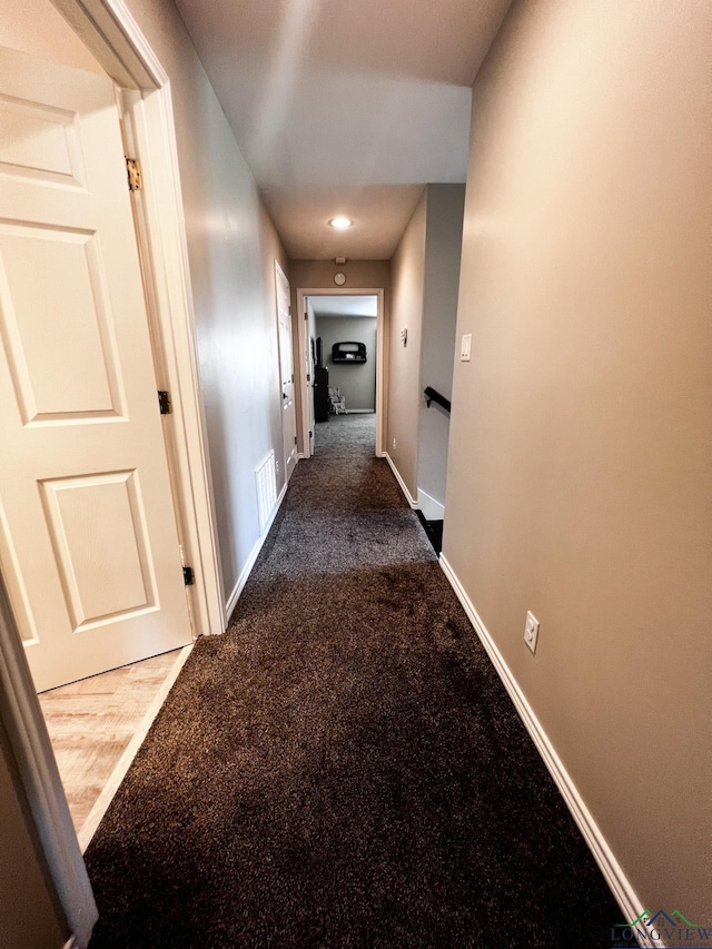 hall with dark carpet, visible vents, and baseboards