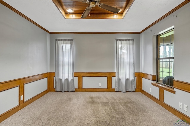 carpeted spare room with crown molding, a ceiling fan, a wainscoted wall, and a tray ceiling