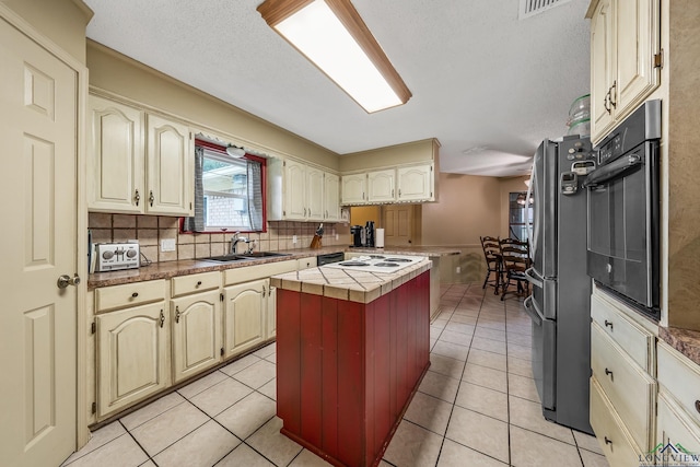 kitchen featuring wall oven, a center island, freestanding refrigerator, light tile patterned flooring, and a sink