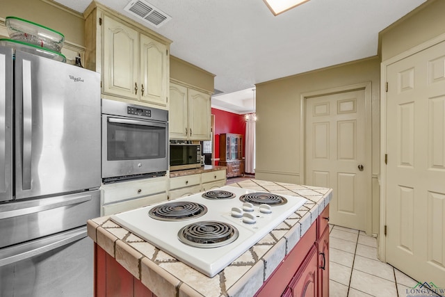 kitchen with visible vents, cream cabinets, stainless steel appliances, light tile patterned floors, and tile counters