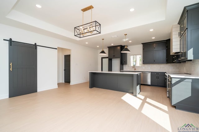 kitchen with a barn door, a kitchen island, appliances with stainless steel finishes, decorative backsplash, and a tray ceiling