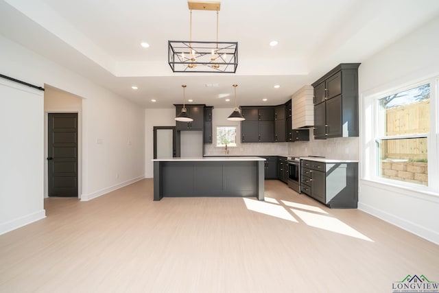 kitchen with a barn door, a kitchen island, stainless steel electric stove, and a tray ceiling