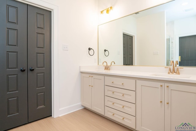 full bath with double vanity, baseboards, a sink, and wood finished floors