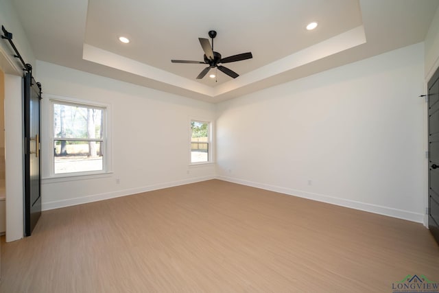 empty room with a barn door, a raised ceiling, and baseboards