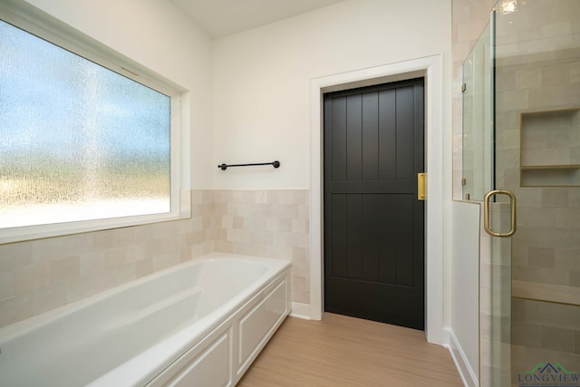 bathroom with a wainscoted wall, a garden tub, tile walls, a shower stall, and wood finished floors