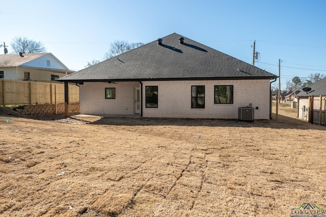 back of property with roof with shingles, brick siding, fence, and central AC unit