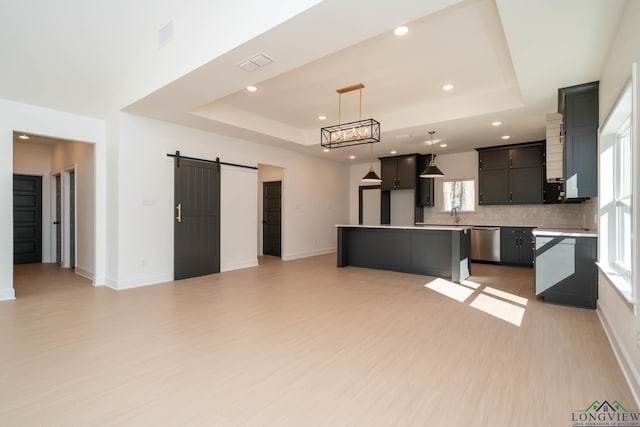 kitchen featuring a barn door, visible vents, backsplash, dishwasher, and a raised ceiling