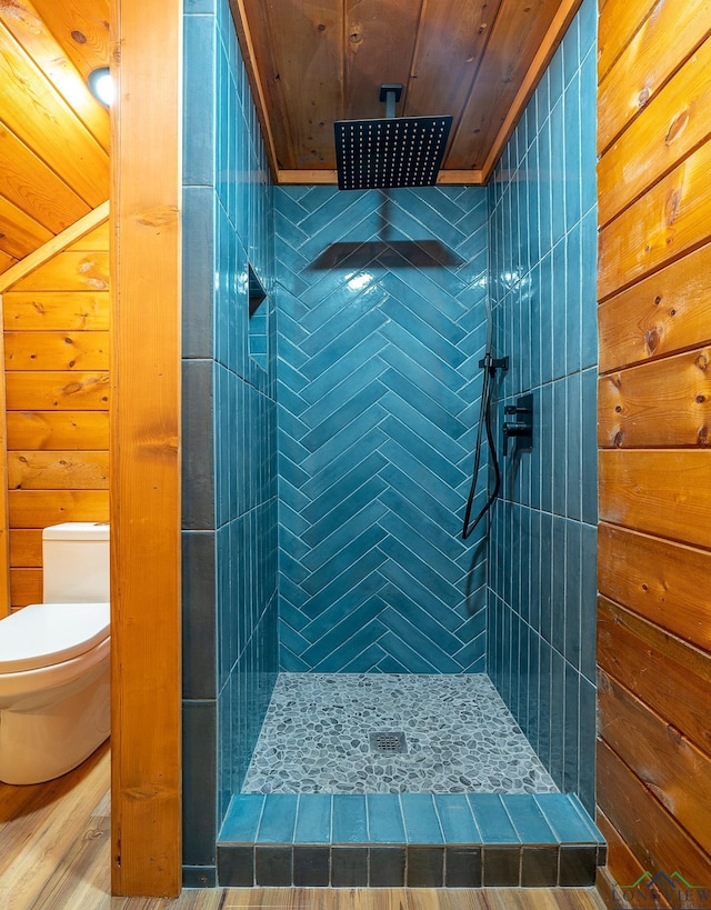 bathroom with toilet, tiled shower, wood walls, and wood ceiling