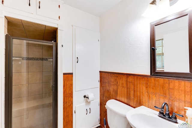 bathroom featuring toilet, a shower with door, wooden walls, and sink