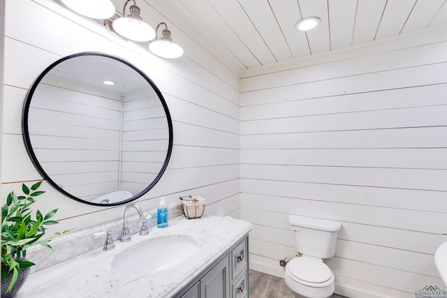 bathroom with wood-type flooring, vanity, toilet, and wood walls