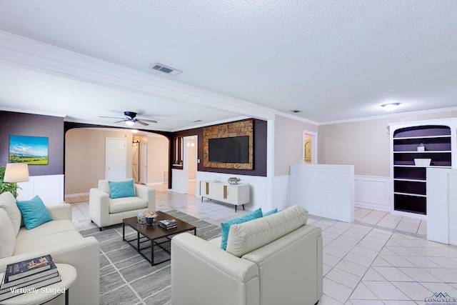 tiled living room with a textured ceiling, ceiling fan, built in features, and crown molding