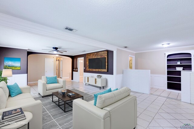 tiled living room with a textured ceiling, ceiling fan, built in features, and crown molding