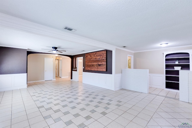 empty room featuring ceiling fan, built in features, ornamental molding, and a textured ceiling