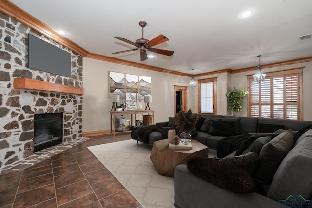 living room featuring dark tile patterned flooring, ceiling fan with notable chandelier, a stone fireplace, and crown molding