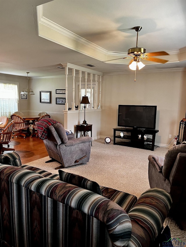 carpeted living room featuring a raised ceiling, ceiling fan with notable chandelier, and ornamental molding