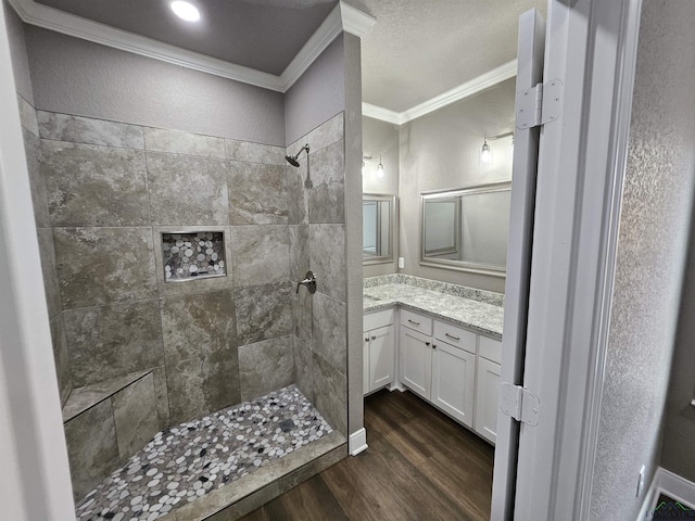 bathroom with crown molding, wood-type flooring, vanity, and tiled shower