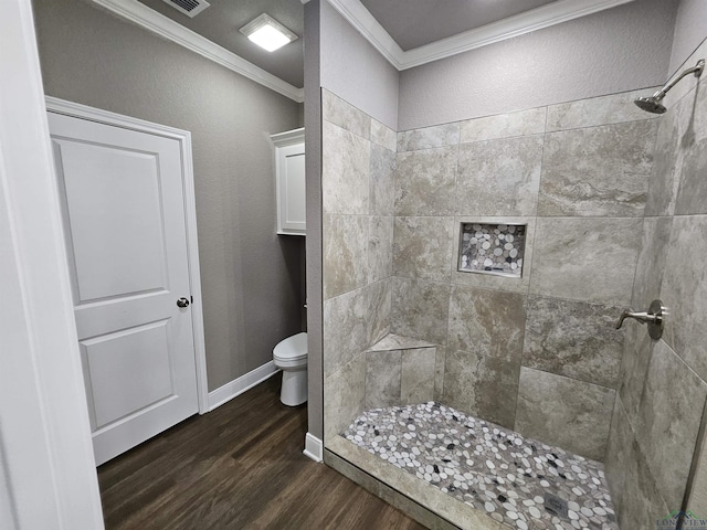 bathroom featuring a tile shower, crown molding, wood-type flooring, and toilet