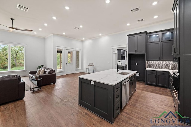 kitchen featuring ceiling fan, sink, light stone countertops, tasteful backsplash, and a center island with sink