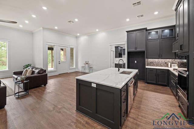 kitchen featuring backsplash, oven, sink, light stone countertops, and an island with sink