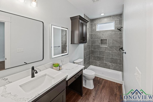 bathroom featuring vanity, toilet, wood-type flooring, and tiled shower