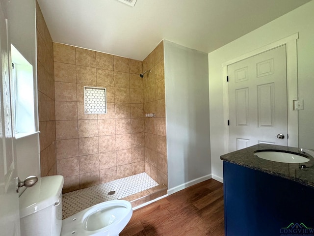 bathroom featuring wood-type flooring, toilet, vanity, and a tile shower