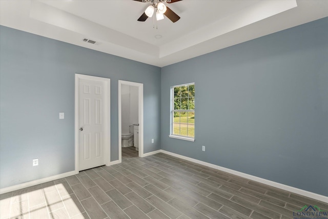 unfurnished bedroom with ceiling fan, connected bathroom, a tray ceiling, and hardwood / wood-style floors