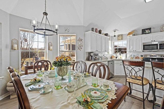 dining room featuring sink, light hardwood / wood-style flooring, a chandelier, and vaulted ceiling