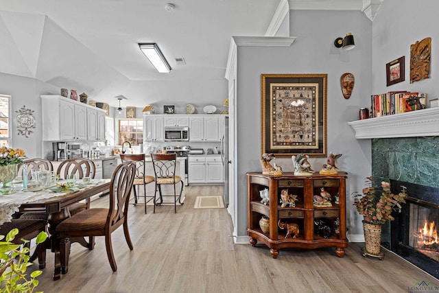 dining area featuring crown molding, vaulted ceiling, light wood-type flooring, a healthy amount of sunlight, and a premium fireplace