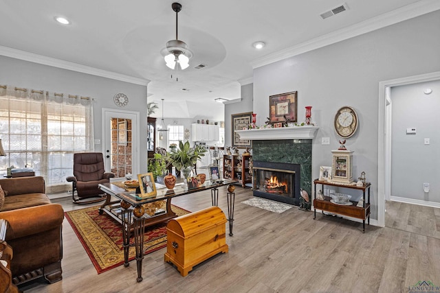 living room with ornamental molding, a high end fireplace, light hardwood / wood-style floors, and ceiling fan