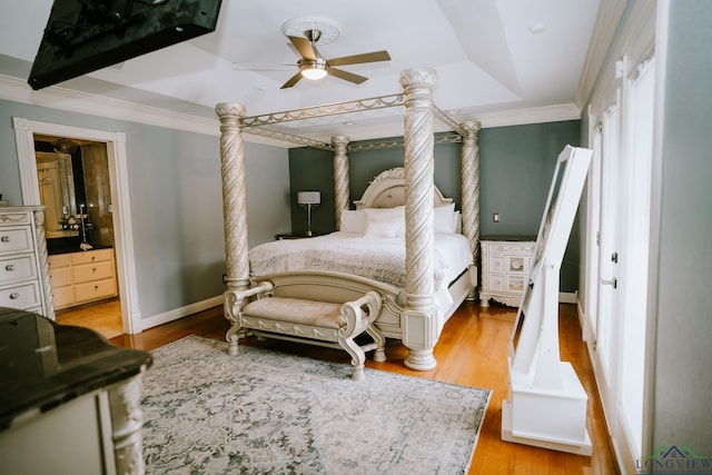 bedroom with connected bathroom, ornamental molding, light hardwood / wood-style floors, and a raised ceiling