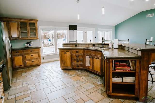 kitchen with stainless steel fridge, a breakfast bar, an island with sink, decorative light fixtures, and vaulted ceiling