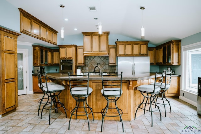 kitchen featuring stainless steel appliances, tasteful backsplash, an island with sink, a kitchen bar, and decorative light fixtures