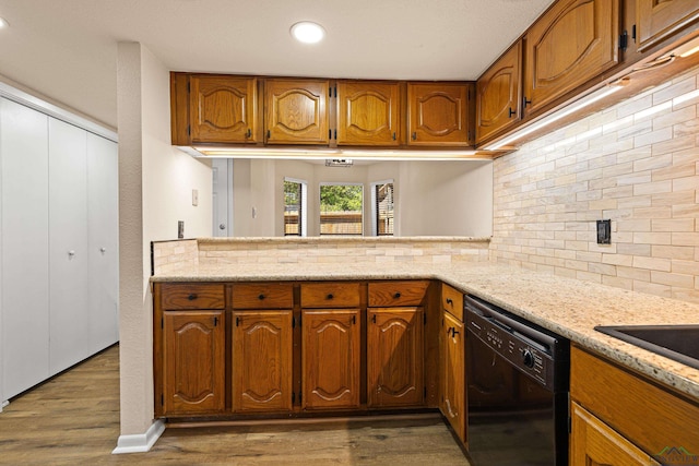 kitchen with brown cabinetry, dark wood-type flooring, black dishwasher, light stone counters, and backsplash