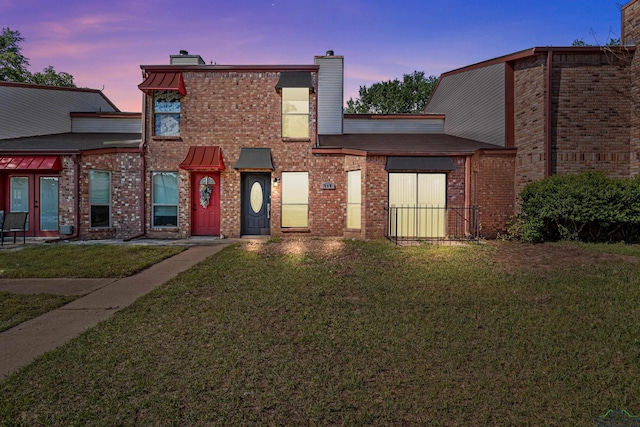 view of front of house with a yard, brick siding, and a chimney