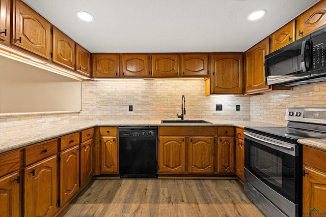 kitchen featuring brown cabinetry, dark wood-style flooring, a sink, and black appliances