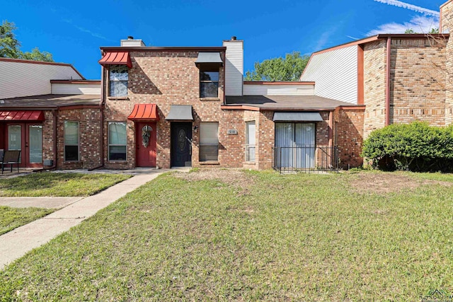 view of front of property featuring french doors, a chimney, a front yard, and brick siding