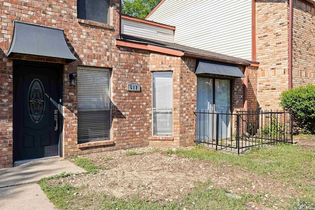 entrance to property featuring brick siding and fence
