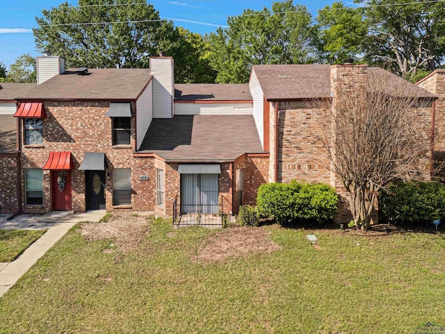 view of front of property with a shingled roof, brick siding, a chimney, and a front lawn