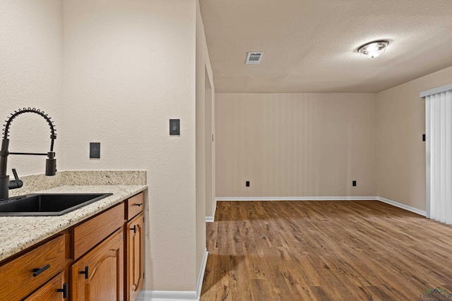 kitchen with brown cabinetry, a textured ceiling, visible vents, wood finished floors, and a sink