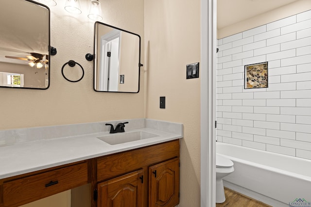 full bath with vanity, a textured wall, toilet, ceiling fan, and wood finished floors