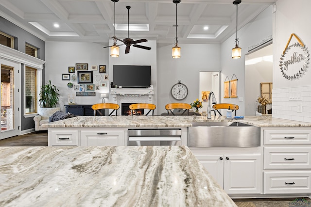 kitchen with white cabinetry, hanging light fixtures, light stone countertops, sink, and a breakfast bar area