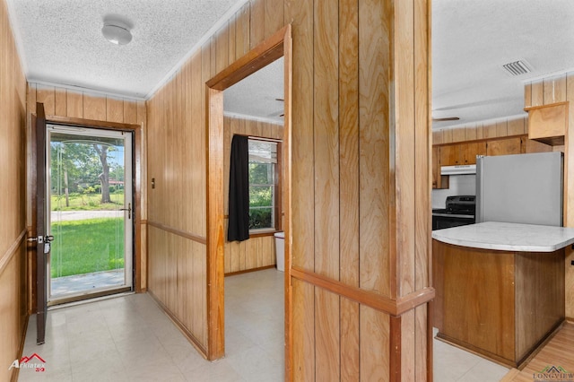 711 Comer St, Carthage, TX 75633 - doorway featuring a textured ceiling, wood walls, healthy amount of natural light, crown molding, and light floors