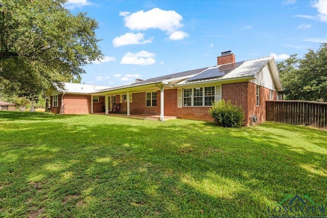 rear view of property featuring a yard, a patio, and solar panels