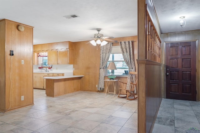 kitchen with kitchen peninsula, a kitchen breakfast bar, ceiling fan, and wood walls