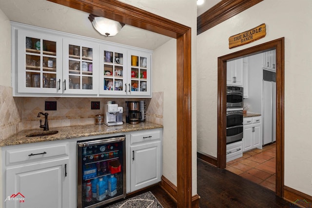 bar featuring sink, wine cooler, light stone counters, decorative backsplash, and white cabinets